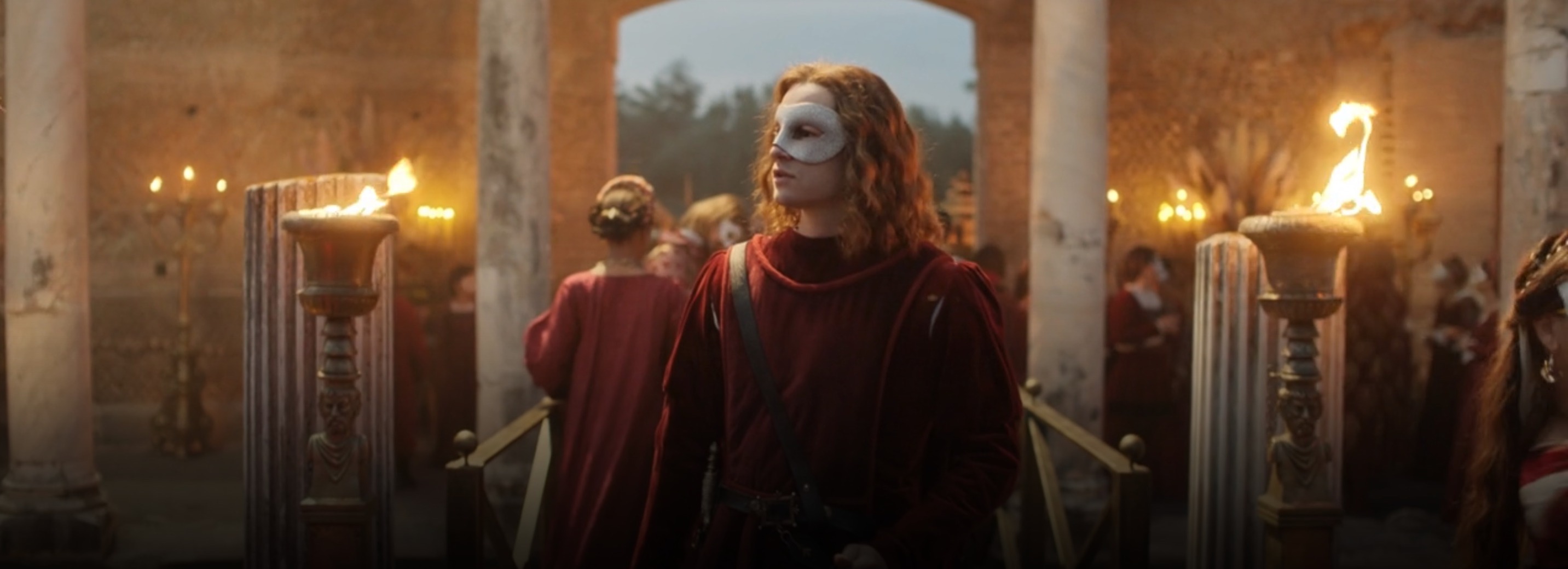 Romeo dressed in red with flame torches behind him, wearing a white mask over his eyes.