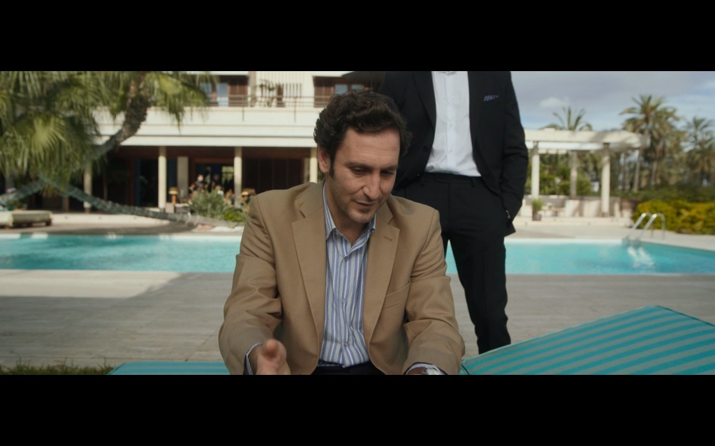 Eduardo wearing a tan suit and sitting on a chaise lounge by the pool.