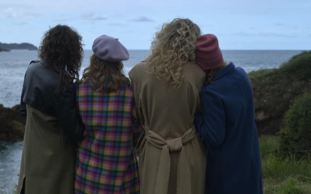 The four friends from the back with arms linked staring out to sea.
