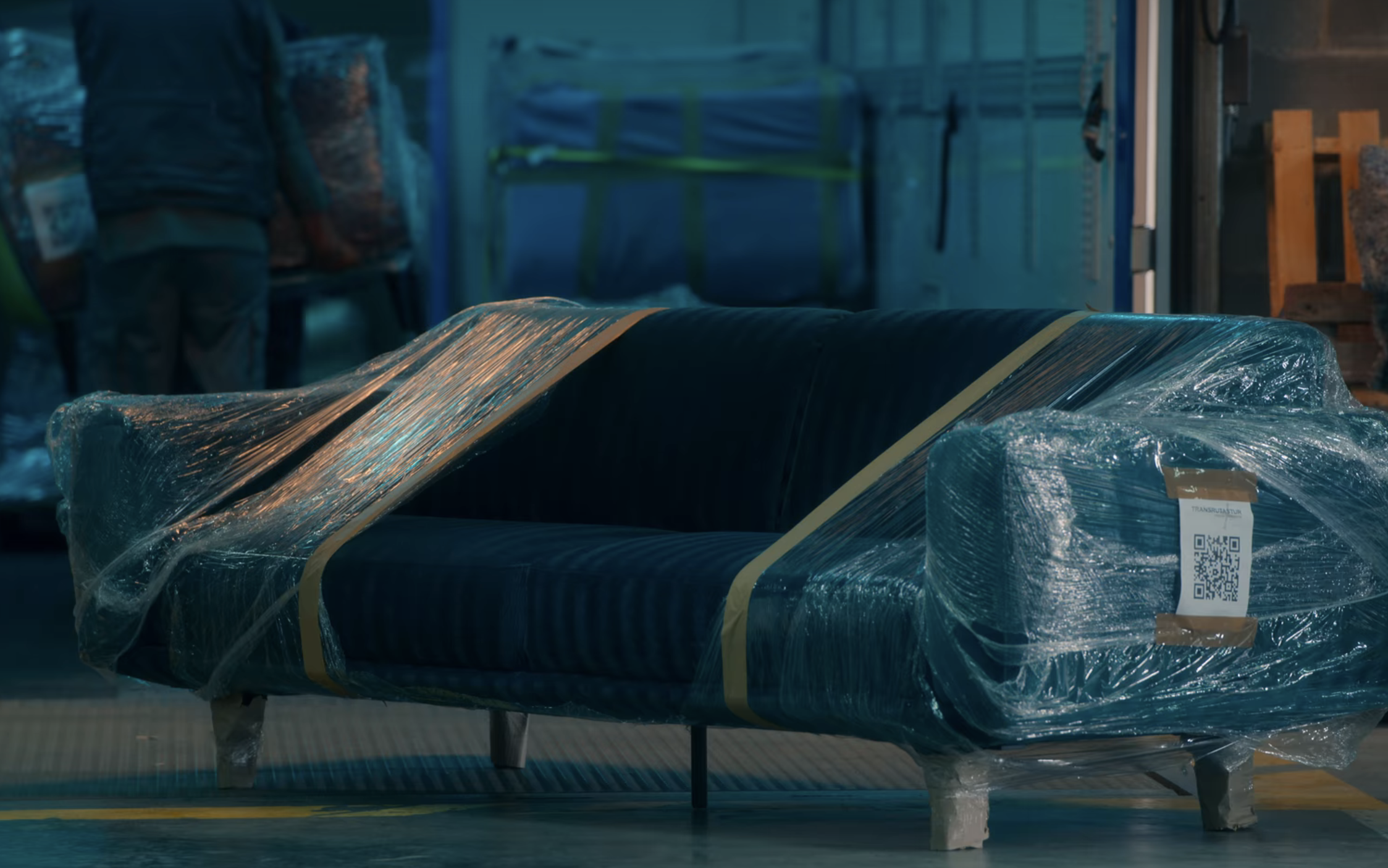 Blue couch partially wrapped in plastic sitting in a warehouse.