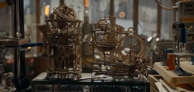 A shot of two wooden contraptions that might be marble runs on a table with windows in the background.